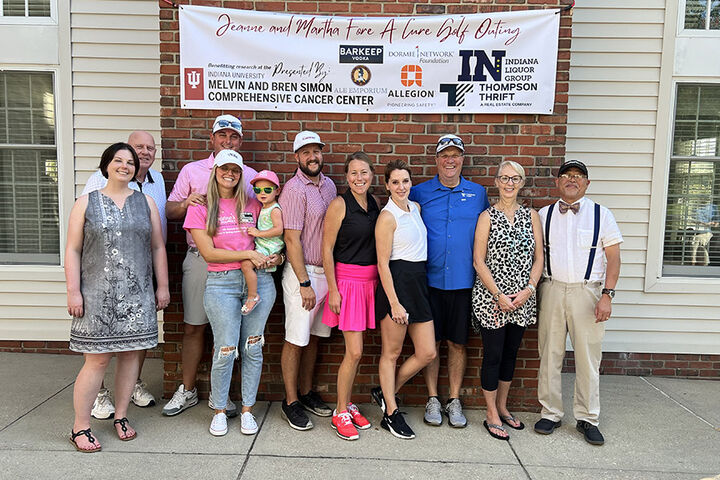 A group of 11 people posing in front of a banner for the Jeanne & Martha Fore A Cure Golf Outing.
